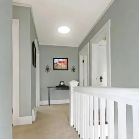 Hallway with a white railing lit by a round tubular skylight