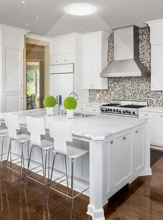 White kitchen with a marble island and bar stools lit by a tubular skylight