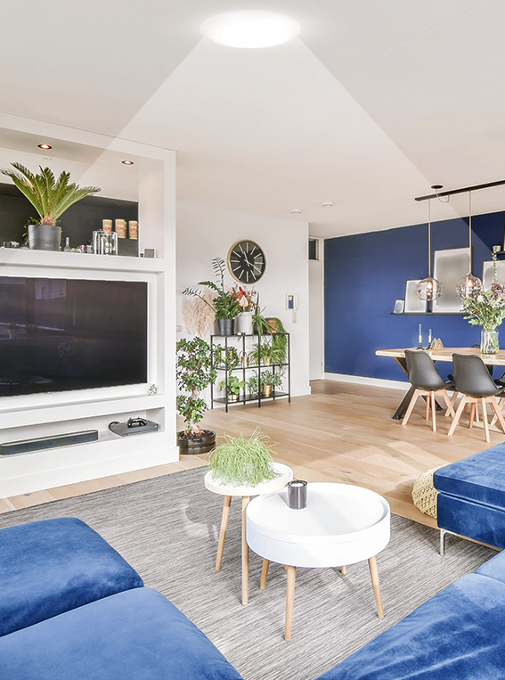 Living room with a blue sectional and TV wall lit by a tubular skylight