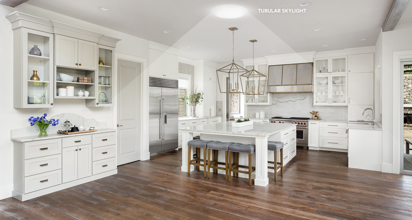 Bright white kitchen and island lit by a tubular skylight in the vaulted ceiling